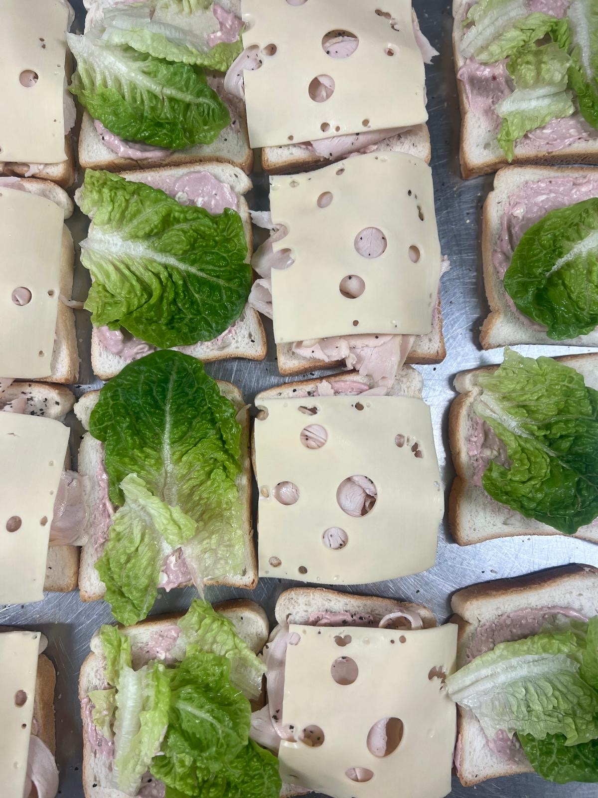 Sliced ham, swiss cheese and cos lettuce sandwiches laid out on a prep tray.
