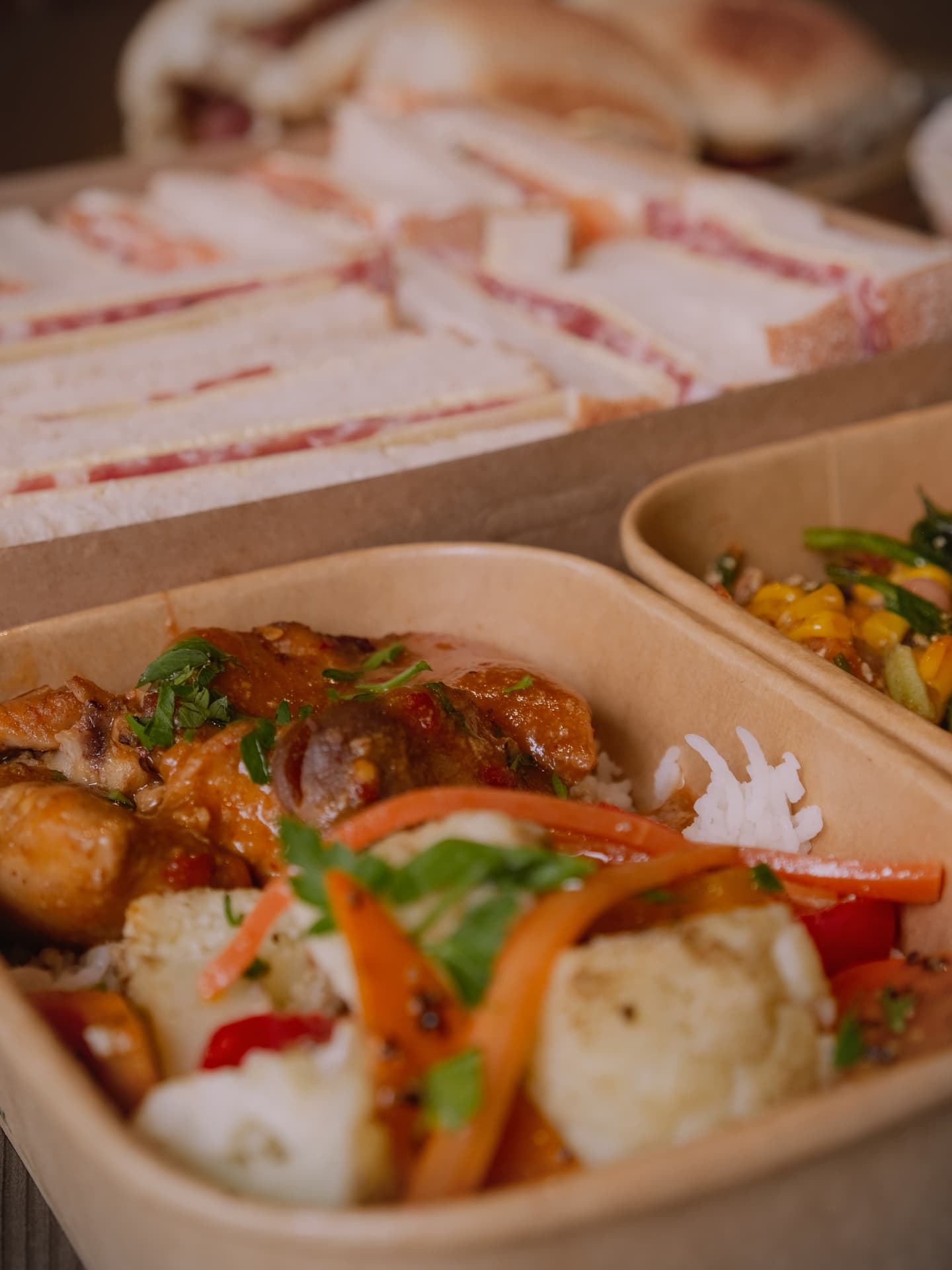 Kraft box of curry, rice and fresh salad beside a tray of ribbon sandwiches.