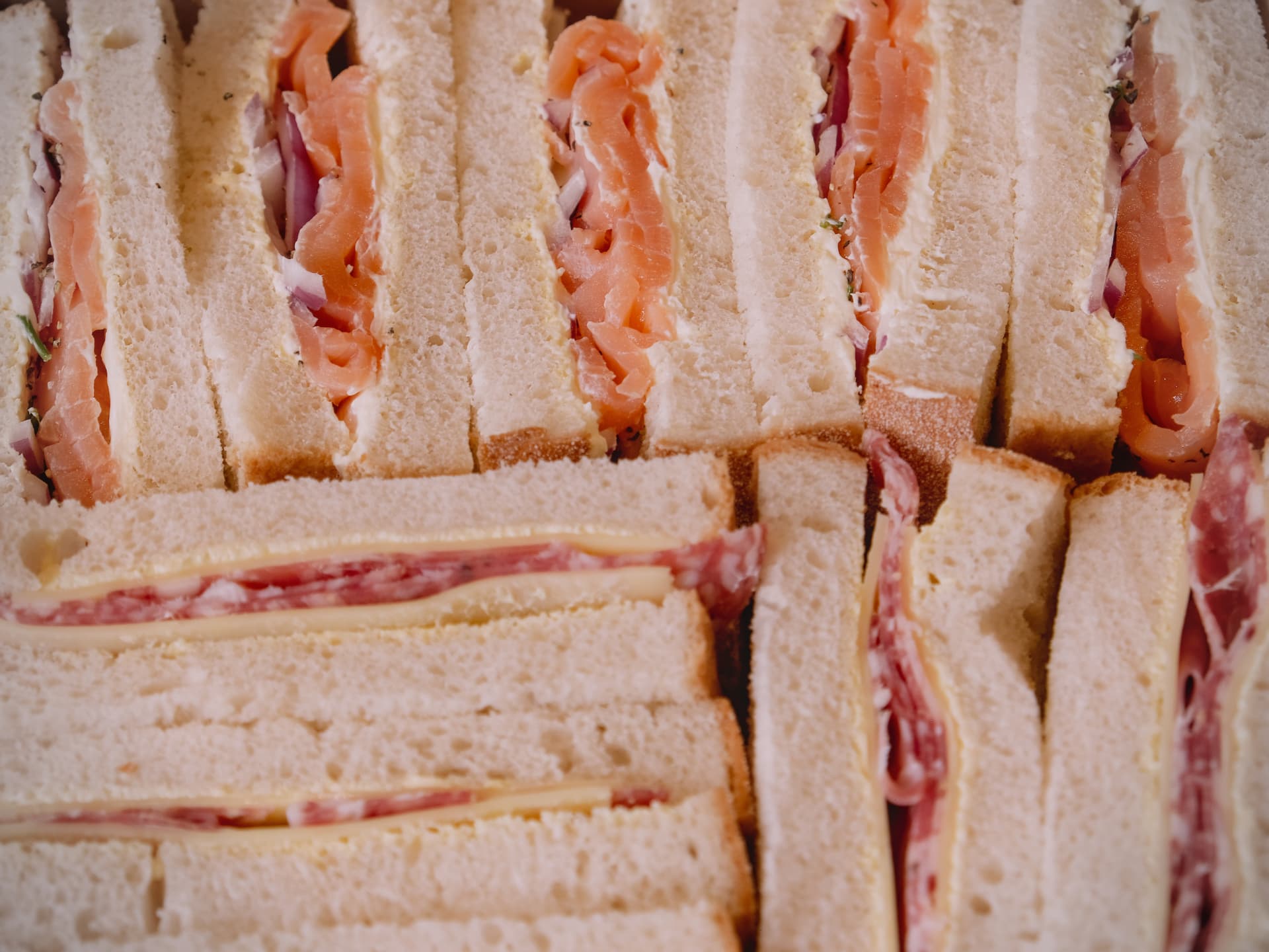 Close up of smoked salmon and salami sandwich points packed side by side.